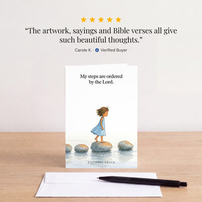 The Ordered by the Lord card on a table with a white envelope. Review: "The artwork, sayings and Bible verses all give such beautiful thoughts." Carole K.