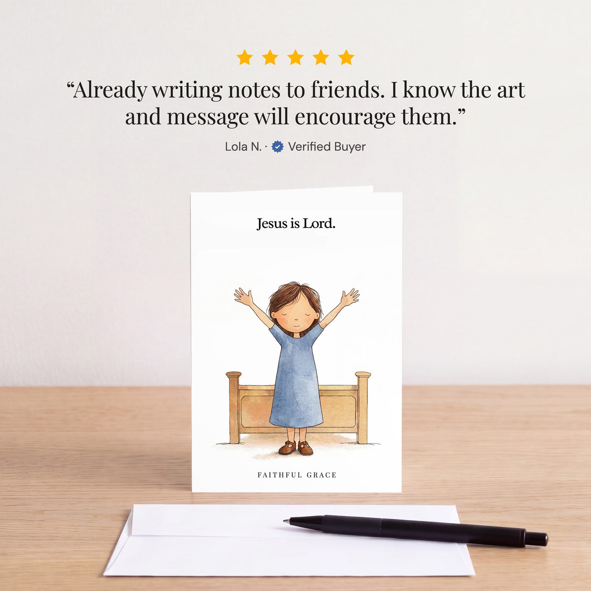The Jesus is Lord card on a table with a white envelope. Review: "Already writing notes to friends. I know the art and message will encourage them." Lola N.